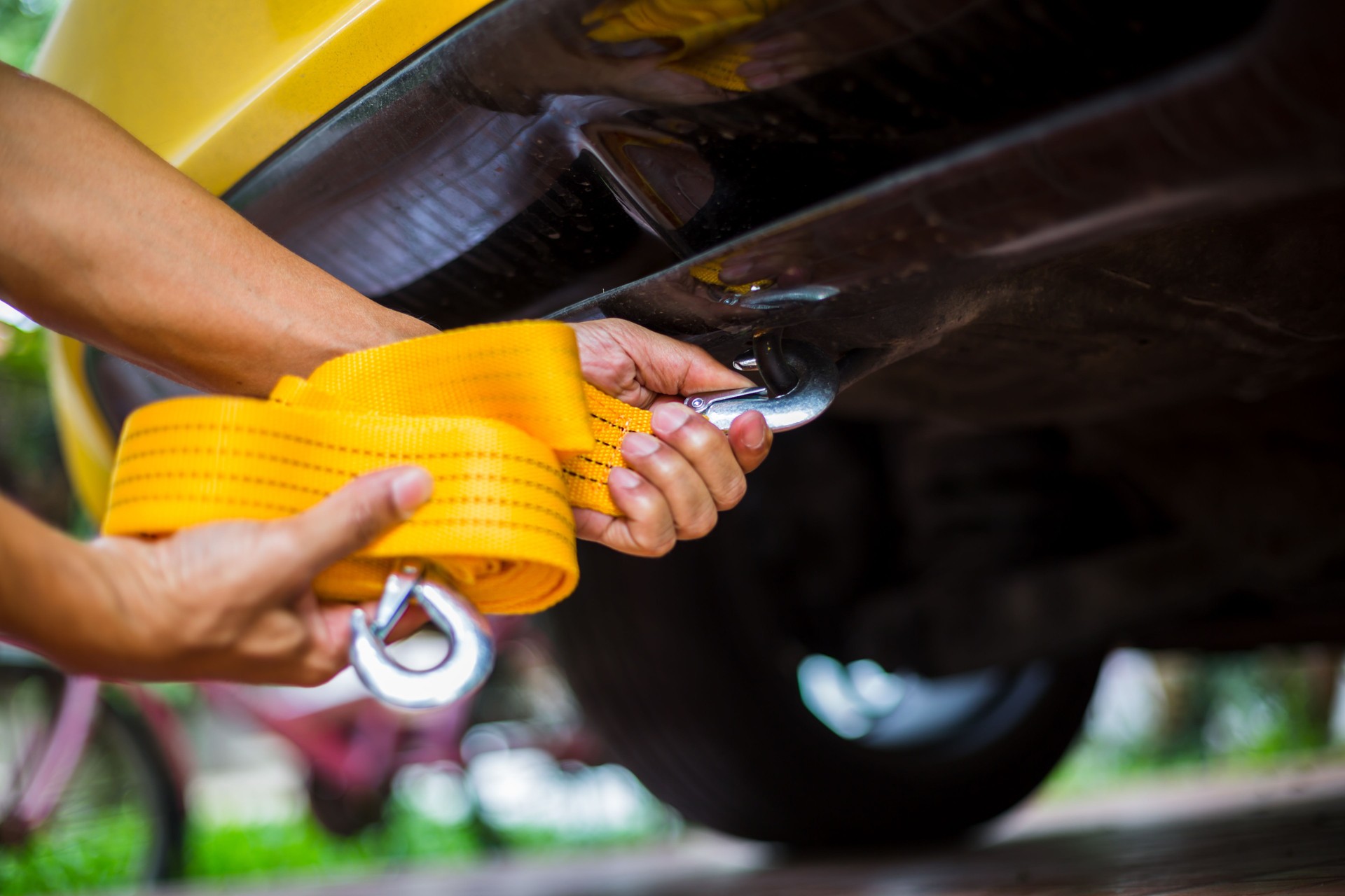 Hands of man holding yellow car towing strap with yellow car.